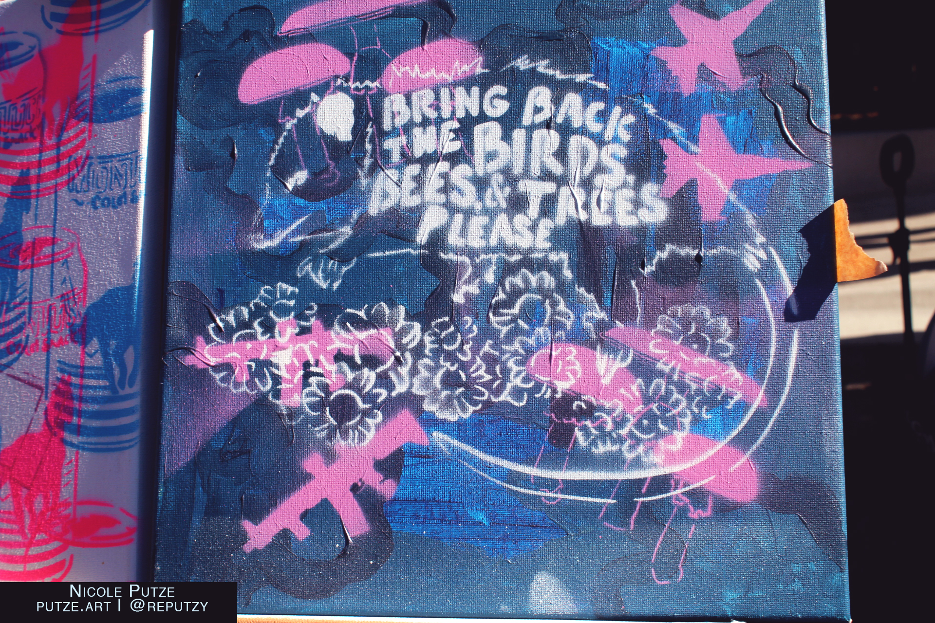 A canvas painting with stencil prints done over top including a possum with "Bring back the birds, bees and trees please!" text inside its body. 
It is surrounded by pink automatic rifles and flowers on a navy blue background. 